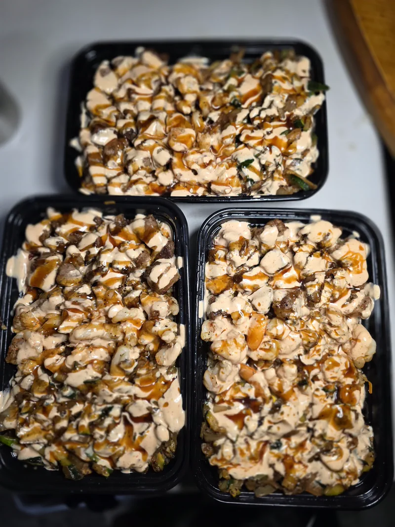 Three sauced hibachi trays lined up side by side, part of one eight-plate batch drop